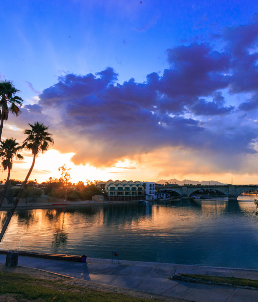 Sunset over Lake Havasu City, Arizona with the London Bridge in the background. Reflections, clouds, and palm trees.